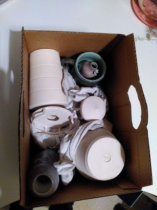 A card box full of pottery wares on top of some fabric cushioning them.
