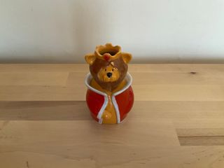 A little vase shaped as a lion wearing a crow set with a red gem and a red coat bordered in white.