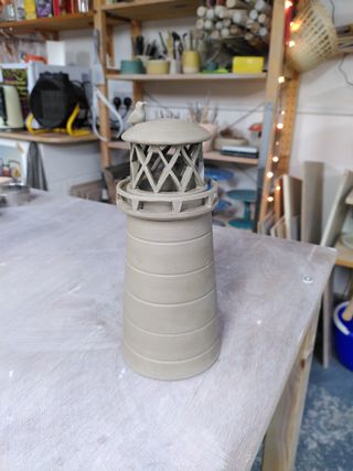 A clay lighthouse with its balcony balustrade and light area carved and a little seagul on top.
