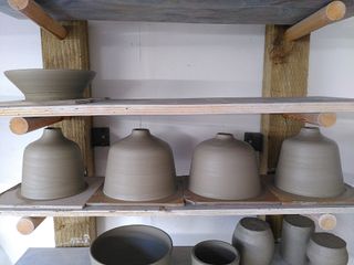 4 bedside table lamp bases, with straight bodies curving into a very short neck, and a bowl waiting to dry on a shelf after throwing