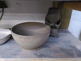 A leather hard trimmed bowl waiting in front of a vase shaped as a sleeping bat.
