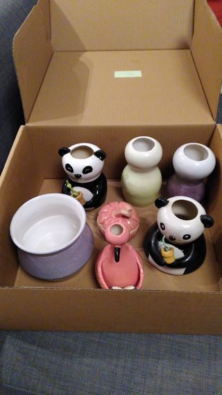 A cardbox with a mix of ceramics: a purple angled planter, two little vases shaped as pandas (one thin, one wider), two little vases glazed respectively in a green and purple gradient, a little pumpkin and a little flamingo bud vase.
