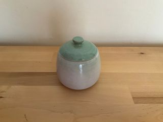 A bubbly lidded jar with a flat knob atop its lid, glazed white outside with a light teal lid and some light teal shading at the rim.