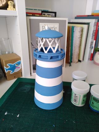 Clay lighthouse painted in underglaze: blue and white striped tower, blue balcony, white carved light setting and blue roof with a seagull sitting on it.