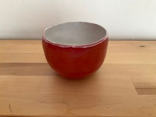 A curvy planter with a white inner glazing dripping on a dark orange outside.