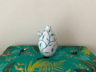 A mini bud vase decorated with a turquoise plant and a sculpted light-grey mouse on its collar.