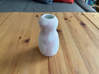 A small 'head and body' vase painted in pink glaze with white brush marks overlaid on it.
