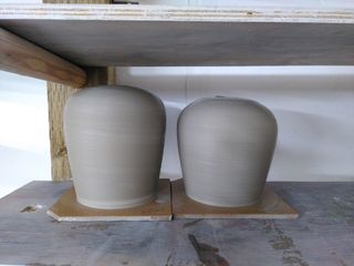 Two clay forms on their bats after throwing, angling outwards up before rounding to a flat top with a small hole.