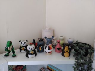 10 character vases amongst a couple more ceramic pieces on a shelf.
