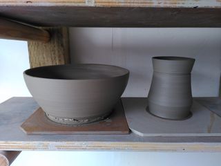 A large bowl and an angular mug body, both in wet clay, on bats after throwing.