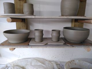 Four clay forms drying on their bat after throwing: a bowl, two cup and another bowl.