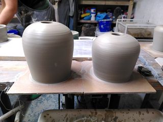 Two clay forms on their bats after throwing, angling outwards up before rounding to a flat top with a small hole.