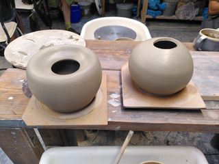 Two clay forms after throwing, with spheric-ish bodies and an opening at the top. Left one's top collapsed down