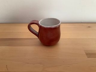 A little cup with a flat handle, its white inside overflowing on a dark red glazing outside.