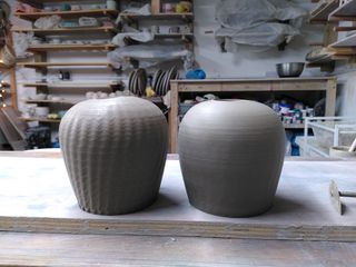 Two clay table lamp bases after trimming, angling outwards up before rounding to a flat top with a small hole. Left one has swirly stripes.