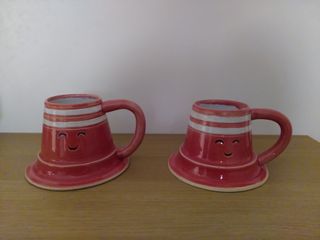 Two mugs in the shape of smiling orange traffic cones with two white bands at the top.