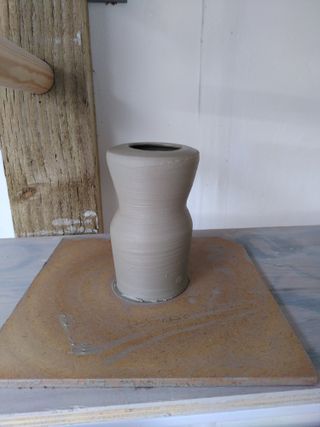 A little vase, clay wet after throwing, with an angular 'head' on top of a lightly slanted reverse-cone 'body'.
