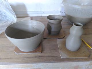 Three clay forms, wet on their bats after throwing: a large bowl, an angular cup body (with medium-large-small segments bottom to top) and a 'head and body' little vase (surmounted of a tiny crown)
