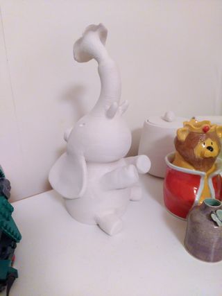 Bisque fired sculpture of an elephant sat on the floor  throwing water up in the air with it trunk.