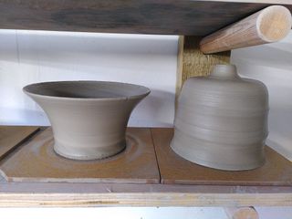 A bowl and bottle like clay forms waiting to dry on a shelf after throwing.