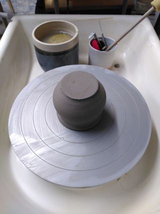Upside down cauldron form on a pottery wheel with a thick amount of clay at its bottom.