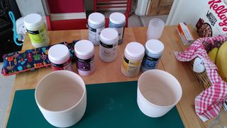 Two planters on a craft mat, in front of a selection of glaze containers.
