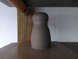 Little stoneware vase shaped as a head on top of a body, its clay still wet after throwing.
